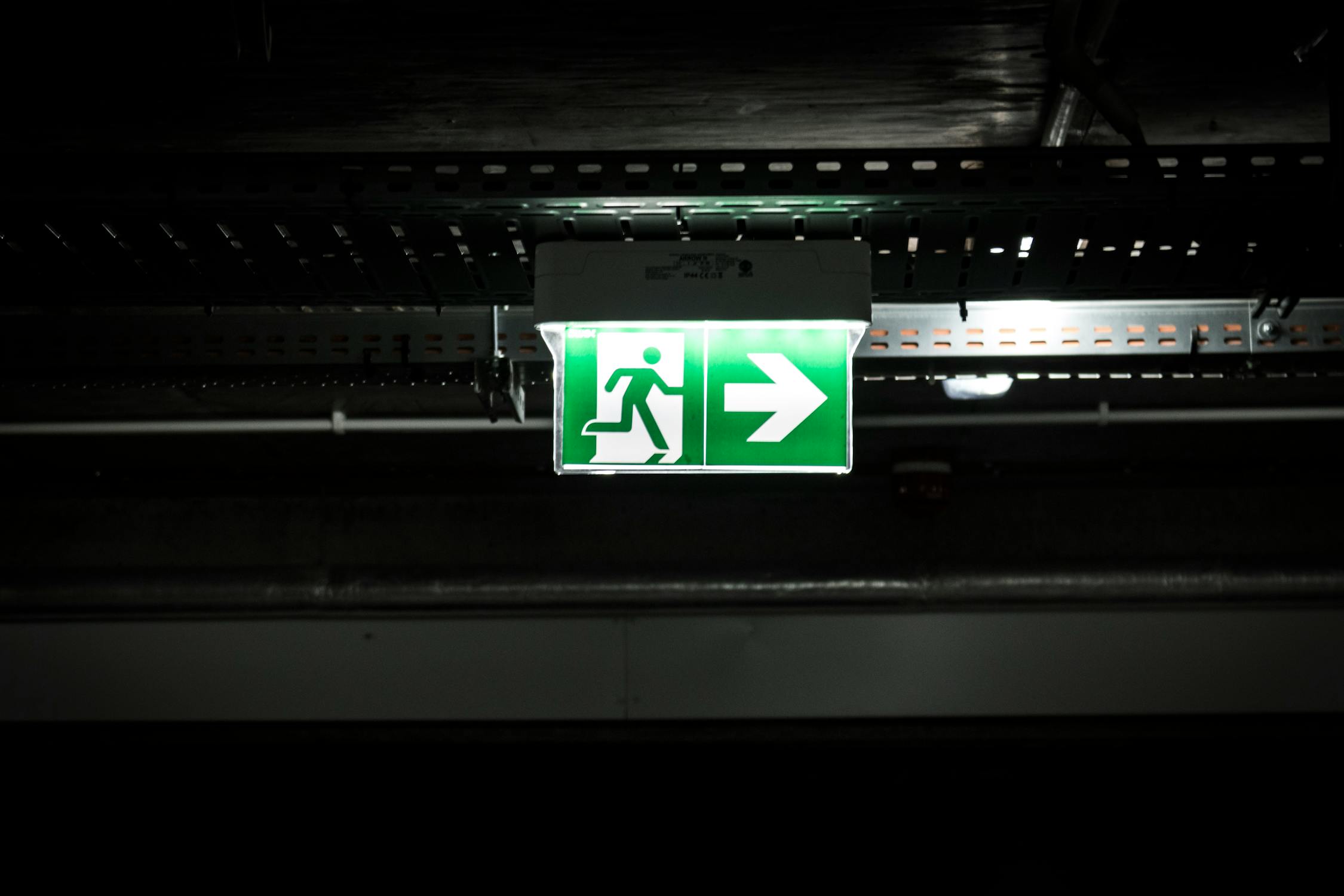 Illuminated green emergency exit sign on dark industrial ceiling