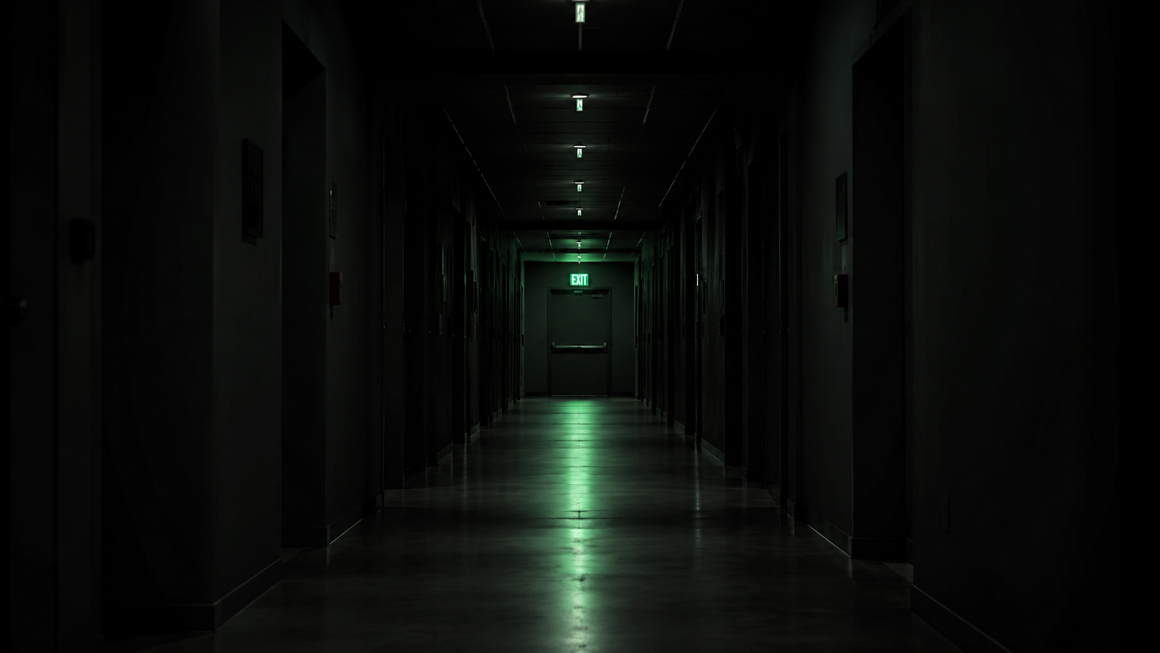 Green LED exit sign above a fire door in a dark commercial corridor — AS 2293 emergency lighting compliance Australia
