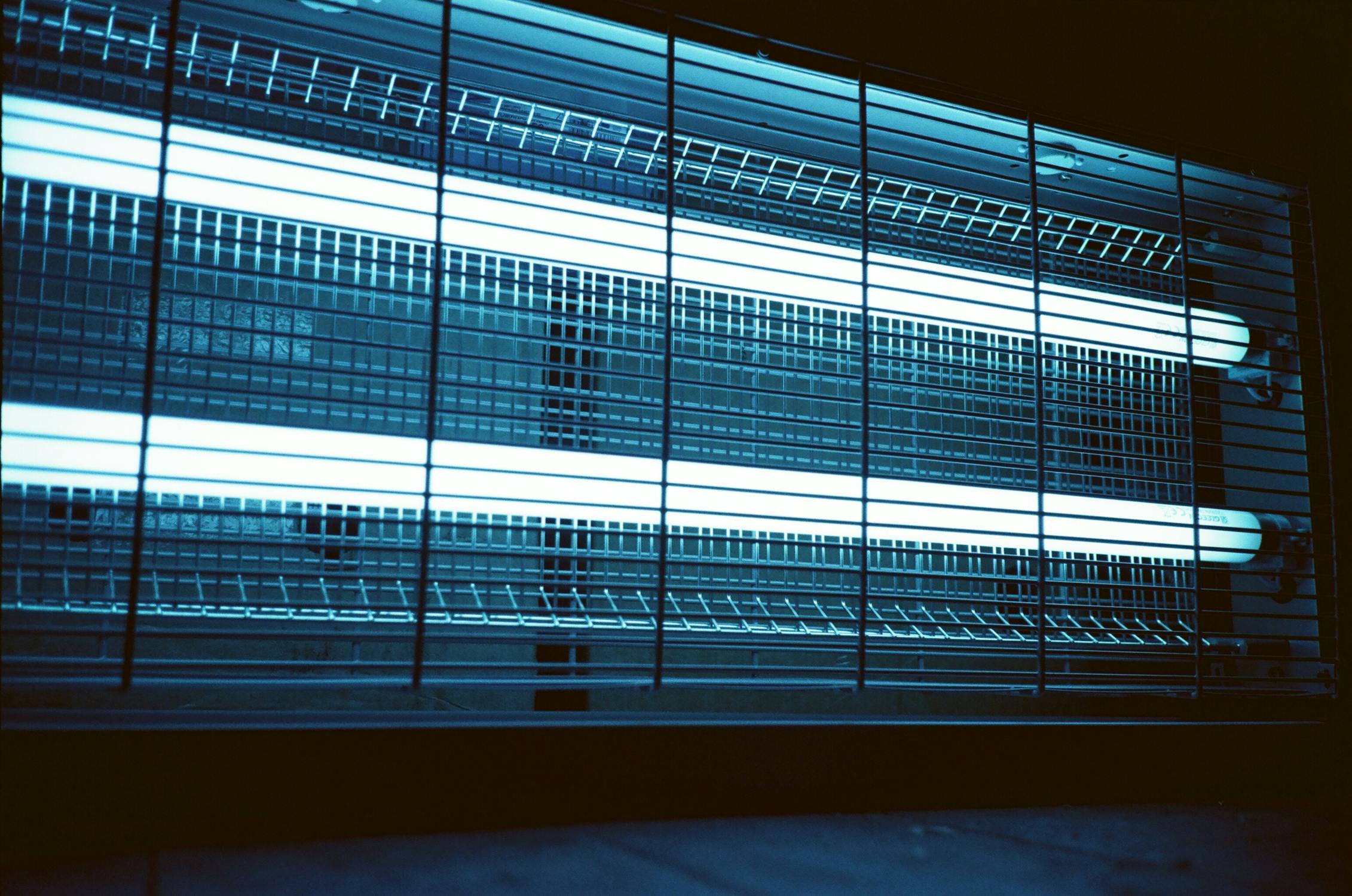 Industrial fluorescent tube lights behind a wire mesh cage guard, the kind being phased out across Australia